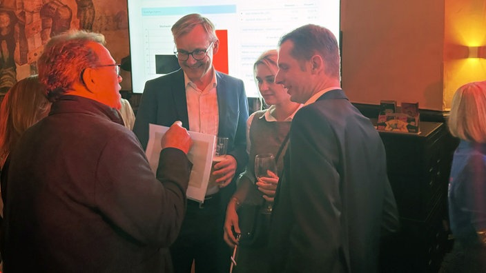 Axel Tschersich unterhält sich mit einer Gruppe von Menschen und lächelt.