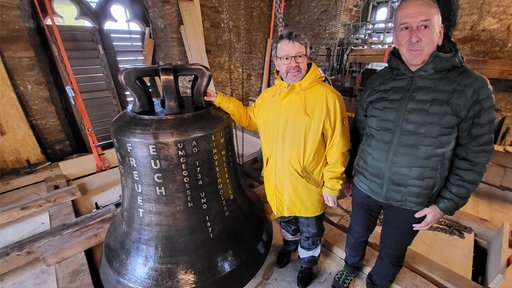 Zwei Männer stehen neben einer großen Glocke