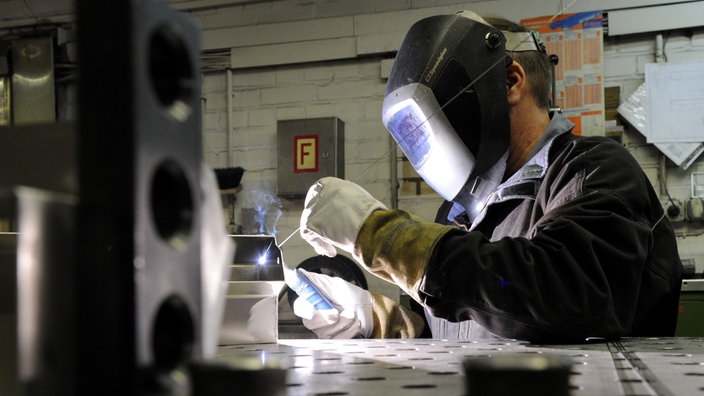 Eine Person mit Schweißermaske, arbeitet an einem Metallgegenstand