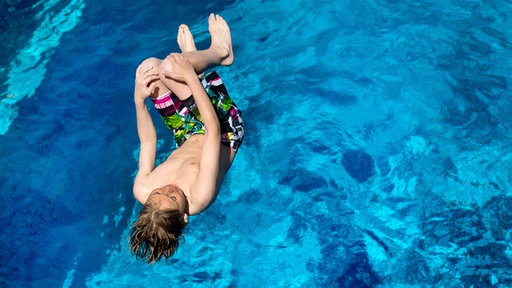 Ein Junge spring im Essener Freibad ins wasser.