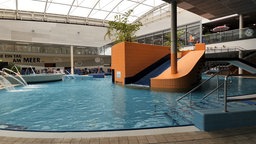 Ein Becken in einem Schwimmbad. Eine Rutsche führt in dieses hinein 