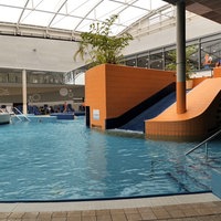 Ein Becken in einem Schwimmbad. Eine Rutsche führt in dieses hinein 