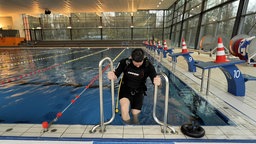 Eine Person in Taucherkleidung steigt in ein Becken, in einem Schwimmbad