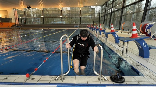 Eine Person in Taucherkleidung steigt in ein Becken, in einem Schwimmbad
