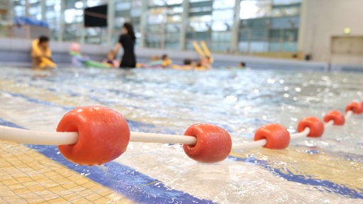 Im Hintergrund schwimmen Kinder im Nichtschwimmerbecken, eine Trainerin steht dabei.