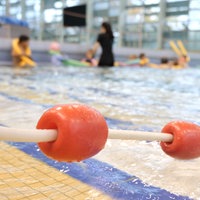 Im Hintergrund schwimmen Kinder im Nichtschwimmerbecken, eine Trainerin steht dabei.