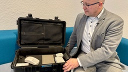Sachverständiger Sascha Puppel vor einem Koffer mit elektronischer Sicherheitssysteme