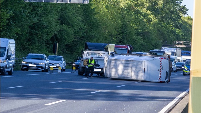 Ein umgekippter weißer Kleinlaster liegt quer auf drei Fahrspuren, ein Mann in Warnweste steht daneben
