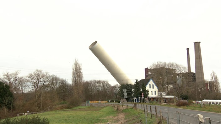 EIn großer Schornstein eines Kraftwerks liegt schief in der Luft, nachdem er kontrolliert gesprengt wurde.
