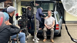 Schauspieler Jörg Hartmann sitzt in einem Auto vor der Kamera