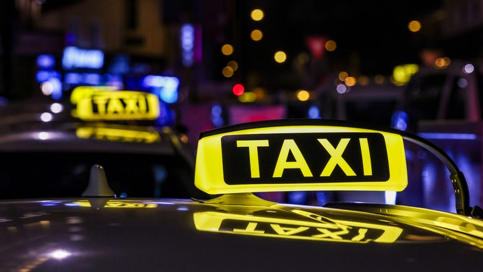 Mehrere Taxis nachts in einer Warteschlange, man sieht in erster Linie das Taxischild