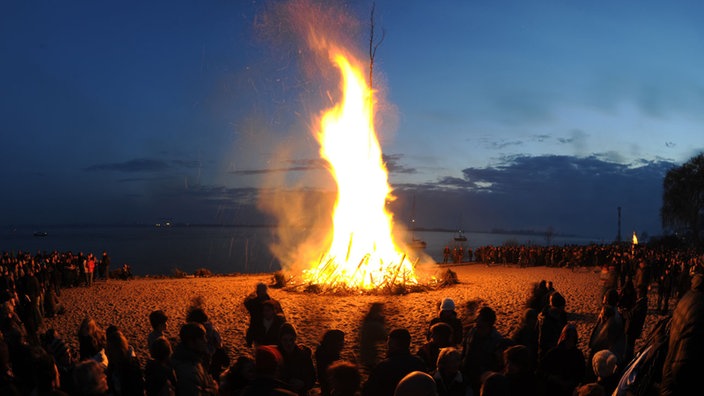 Ein großes Osterfeuer am Strand mit vielen Menschen 