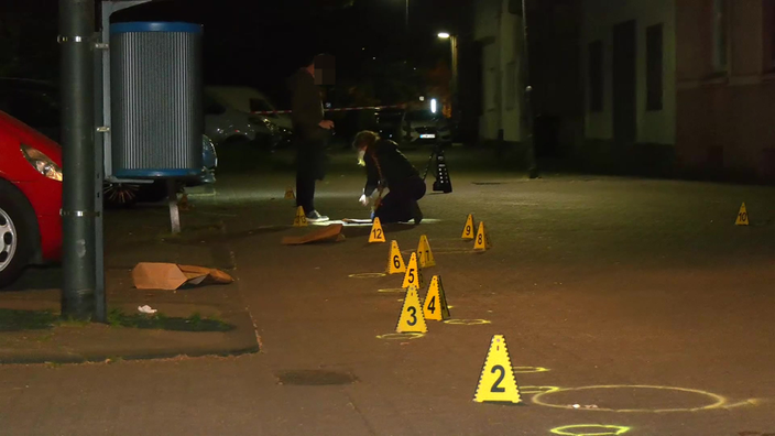 Zwei Personen der Spurensicherung markieren in Duisburg einen Bereich auf einer Straße mit gelben, nummerierten Kegeln.