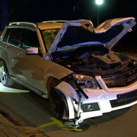 Ein beschädigter SUV mit offener Motorhaube, vorne klemmt ein E-Roller unter dem Fahrzeug