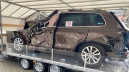 Ein Autowrack welches Vorne eingedrückt ist , steht auf einer Art Podest in einem Zelt
