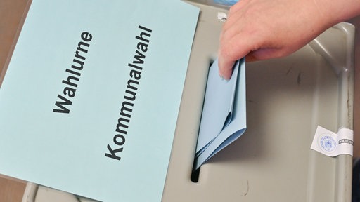 Ein roter und ein gelber Wahlzettel und ein Stift liegen auf einem Holztisch
