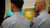 Zwei Polizisten vor einem Bildschirm im Fernsehstudio der Lokalzeit aus Dortmund
