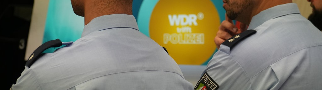 Zwei Polizisten vor einem Bildschirm im Fernsehstudio der Lokalzeit aus Dortmund