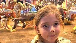 Ein kleines Mädchen steht vor einem Karussel