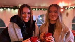 Zwei Frauen stehen an einem Tisch und haben eine Tasse in der Hand