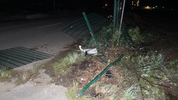 Ein kaputter grüner Zaun neben einer Straße bei Nacht.