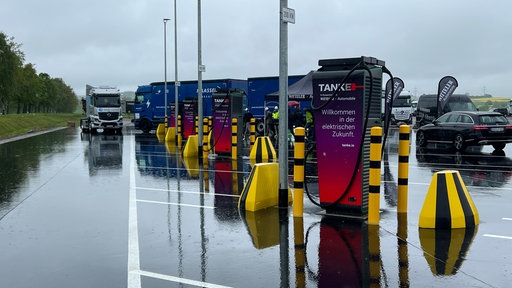 Mehrere Ladestationen für E-LKW auf einem Parkplatz. LKWs und Autos sind im Hintergrund.