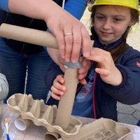 Zwei Kinder basteln mit Papprollen und tragen gelbe Bauhelme.