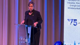 NRW-Wirtschaftsministerin Mona Neubaur steht auf der Bühne und spricht in ein Mikrofon