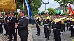 Männer in Anzug und Uniform, manche halten fahnen hoch