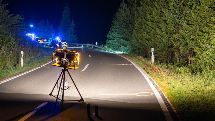 Kurz vor der Kurve auf einer Landstraße ist ein Polizeilicht aufgestellt, in der Kurve sind Polizeiautos zu sehen.