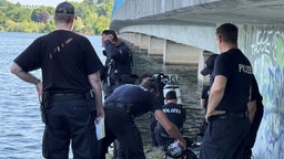 Polizeibeamte stehen unter einer Brücke des Möhnesees und haben Tauchausrüstungen dabei.