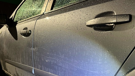 Ein silbernes Auto bei dem die Tür zerkratzt ist.