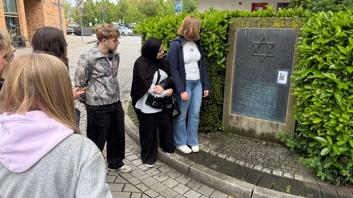 Jugendliche schauen sich die Gedenktafel zur abgebrannten Synagoge in Iserlohn an