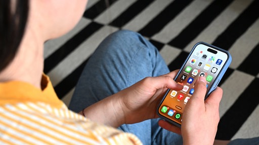 Eine Jugendliche sitzt auf dem Boden und hält ein Smartphone in der Hand