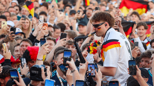 Gute Stimmung beim Public Viewing in Oberhausen. Ein Mann mit Sonnenbrille und Deutschlandtrikot spielt in Mitten von jubelenden Fans Saxophon.