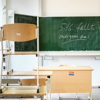 Ein leeres Klassenzimmer mit hochgestellten Stühlen und einer Tafel mit Schriftzug "5./6. fällt morgen aus!"