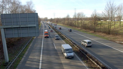 Mehrspurige Autobahn mit fließendem Verkehr, mehrere Autos und Transporter fahren durch eine ländliche Umgebung.