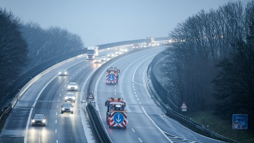 Mehrspurige Autobahn mit Verkehr bei Nebel, zwei Straßenmeisterei Fahrzeuge sichern eine Fahrbahn