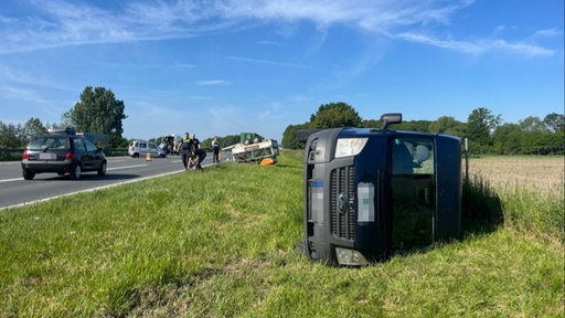 Ein schwarzer Transporter liegt seitlich auf der Wiese neben der Fahrbahn. Im Hintergrund sind ein Anhänger und zwei weitere Fahrzeuge.