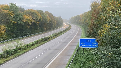Die leere Autobahn A59 in einer bewaldeten Landschaft, am Rand ein Schild Richtung Köln und Leverkusen.