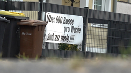 Protestplakat an einem Gartenzaun in Sechtem. Darauf steht: "Über 600 Busse pro Woche sind zu viele!" Im Bild außerdem ein dunkles Auto und mehrer Mülltonnen.