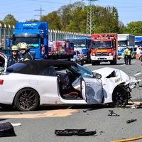 Ein stark beschdigtes, weißes Auto auf der autobahn, drumherum Rettungwagen und Polizei
