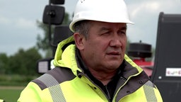 Arif Doruk, Bauleiter Windpark Alpen-Veen, schaut in Arbeitskleidung mit Helm und Warnjacke über die Baustelle.