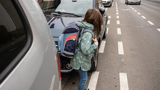 Ein Kind mit Schulranzen auf dem Rücken will eine Straße überqueren