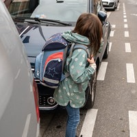 Ein Kind mit Schulranzen auf dem Rücken will eine Straße überqueren