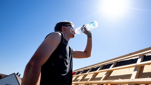 Ein Dachdecker trinkt Wasser unter der sengenden Sonne bei über 30 Grad auf dem Dach eines Hauses