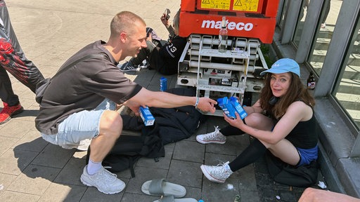 Hitzehelfer verteilt Wasser an eine lächelnde Frau.