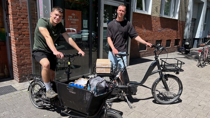 Zwei Männer stehen mit ihren Fahrrädern und den Hilfsgütern auf dem Bürgersteig.