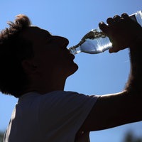 Silhouette eines Mannes, der aus einer Wasserflasche trinkt, im Hintergrund blauer Himmel