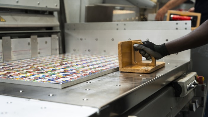 Die Panini-Sticker in der Druckerei. Rechts im Bild sieht man eine Hand, die eine Holzpresse hält.